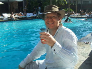 Author Luke Wiliams holding a drink by a pool and wearing a hat totally chilling out