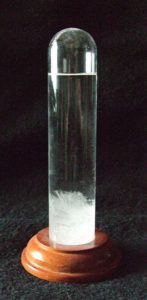 a vertical glass tube on a wooden base, with a white froth of chemical crystals in the bottom
