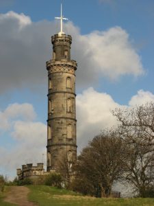 A round stone tower of five stories with a cross-shaped support pole on the roof with a gold time ball resting at its base. The Nelson Tower in Edinbourgh
